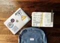 flat lay photography of blue backpack beside book and silver MacBook