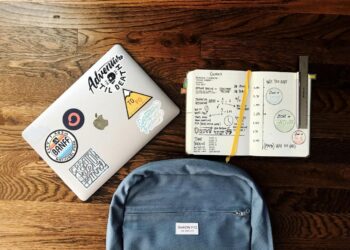 flat lay photography of blue backpack beside book and silver MacBook